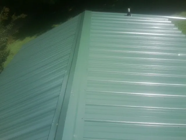 New green metal panels meeting at the ridge of a roof — Flat Roof Repair work by our crew in Minden