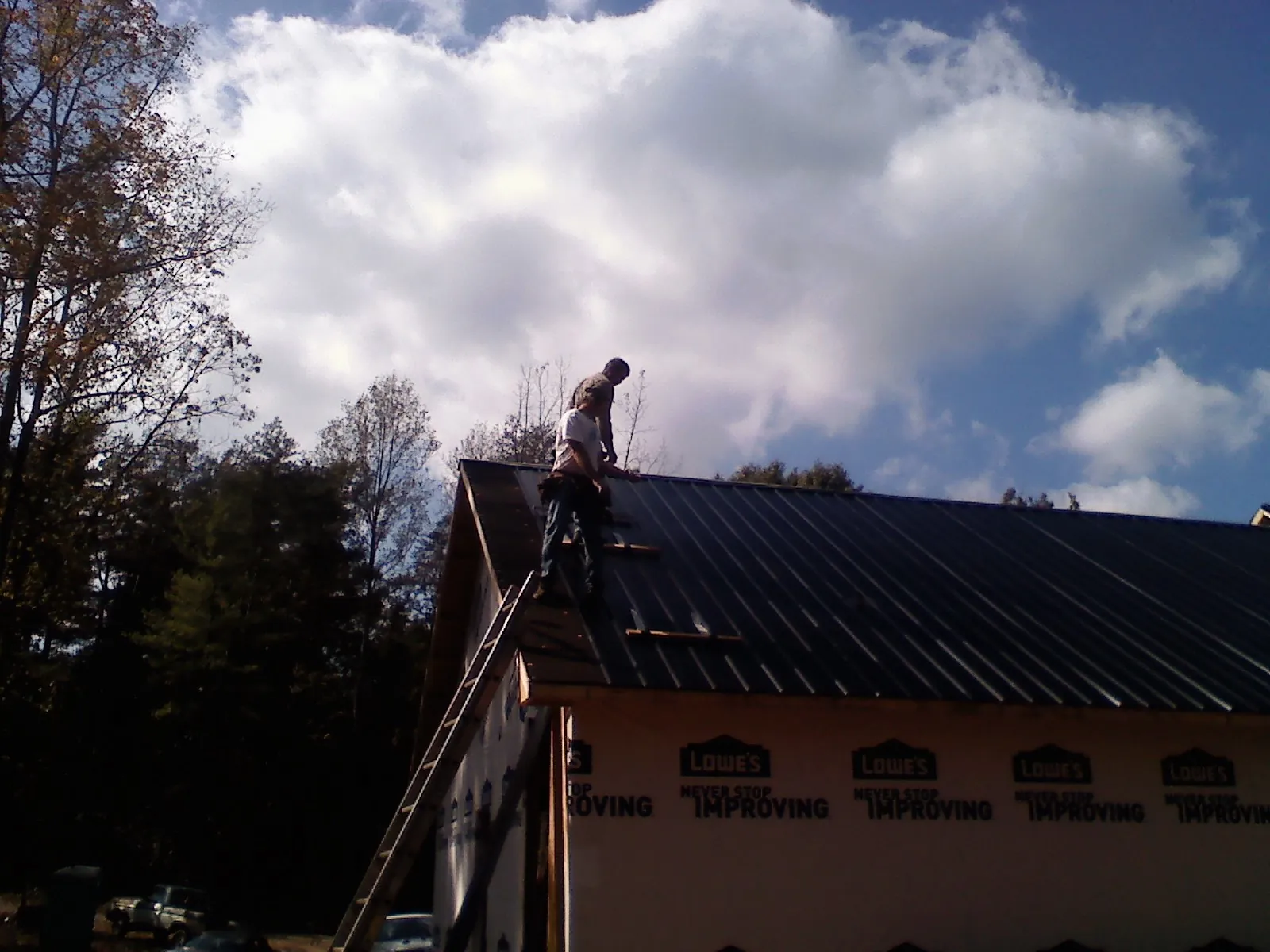 Roofer fastening dark metal panels high against a cloudy sky, from a Roof Inspection job in Minden