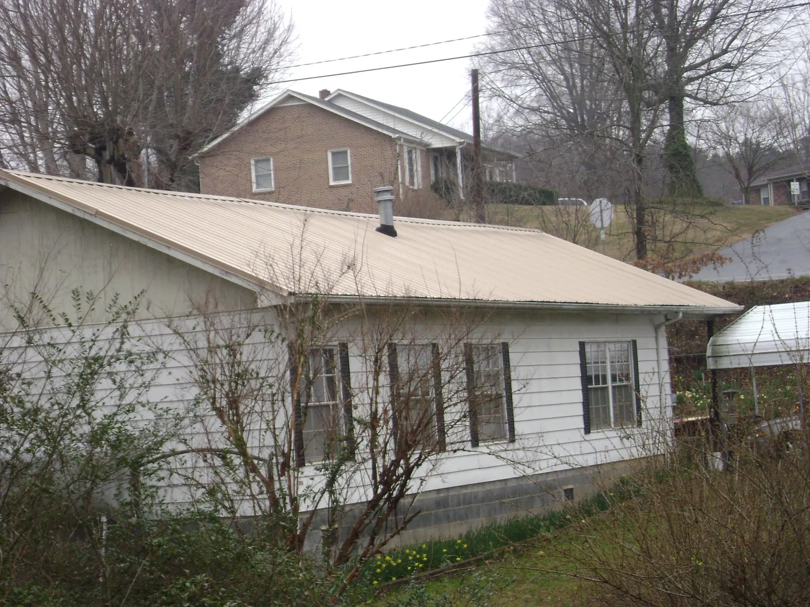 Tan metal roof on a white sided house set into a hillside — Commercial Roofing by Roofing Brothers in Minden