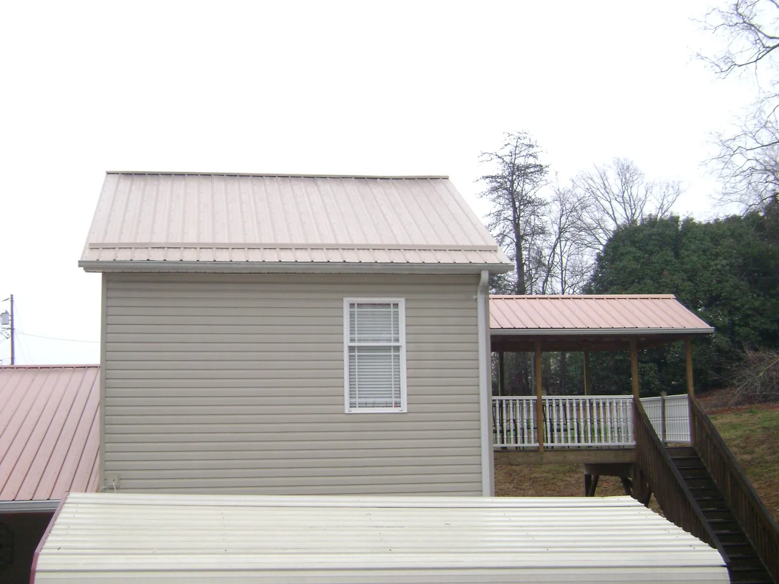 Tan metal roofs on a two story addition and attached porch, from a Roof Replacement job in Minden
